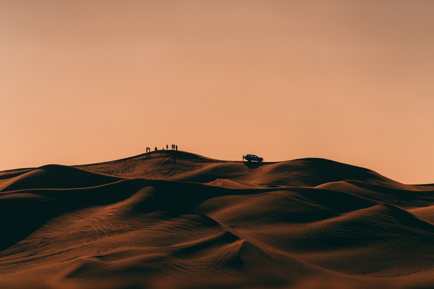 Desert dunes at sunset with figures silhouetted on the ridge